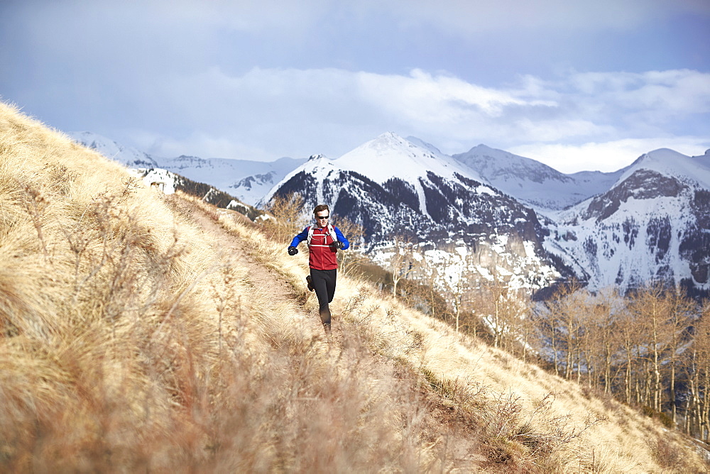 Adult male trail running through a grassy trail high in the mountains above Telluride Colorado on a beautiful spring afternoon, Telluride, Co, USA