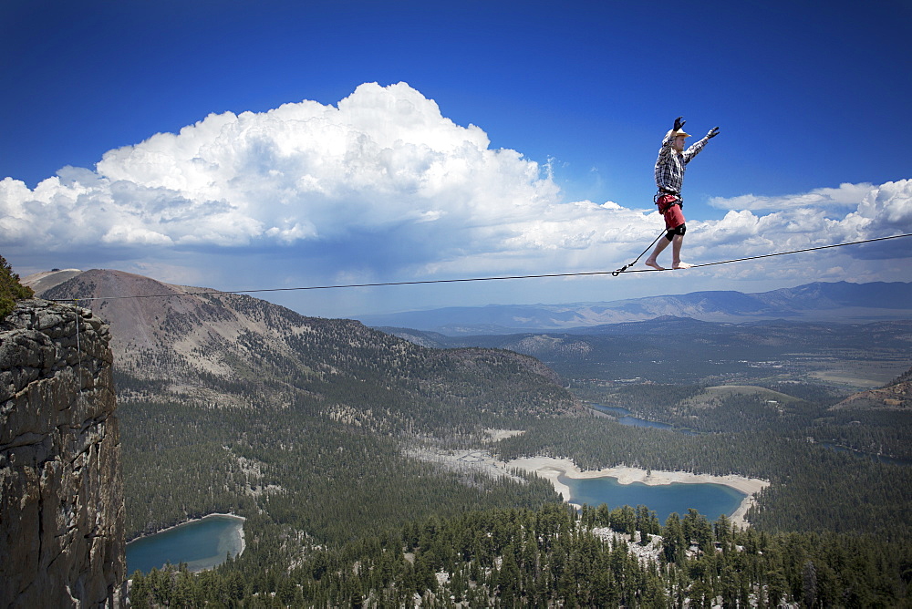 Male highliner in cowboy hat walks a 125 foot highline over a lake in a gap on top of Mammoth Crest, Mammoth, California, United States