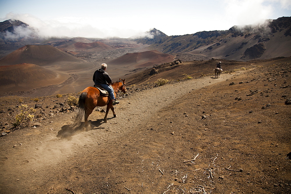 Two men on horseback ride into Haleakala crater, Maui, Hawaii, United States of America