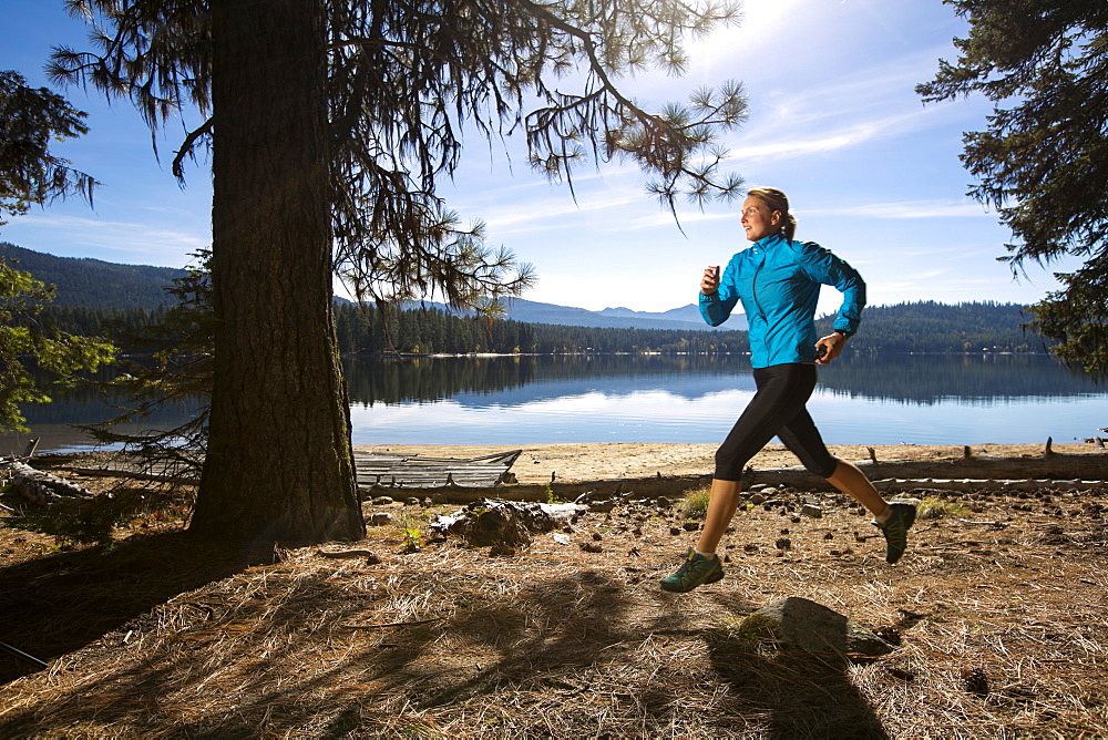 A female trail runner running next to Payette Lake in Ponderosa State Park, McCall, Idaho in the fall, Ponderosa State Park, McCall, Idaho, USA