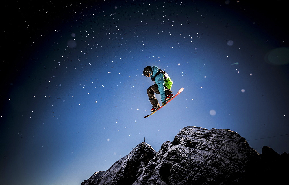 A snowboarder leaping into the air on the Dachstein-Glacier in Austria, leaving a trail of snow behind him.