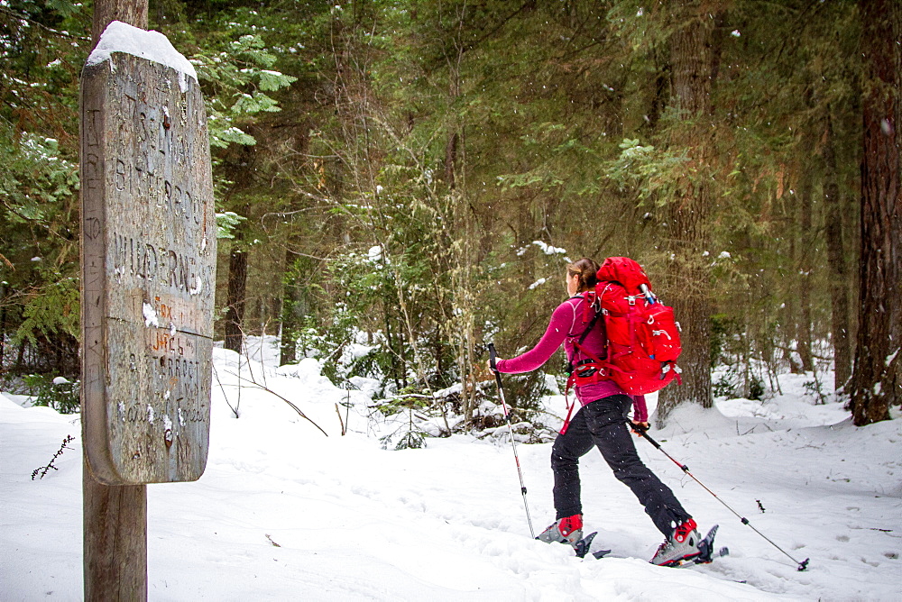 A woman backcountry skier skis by a sign marking the beginning of the Selway-Bitterroot Wilderness in Montana.