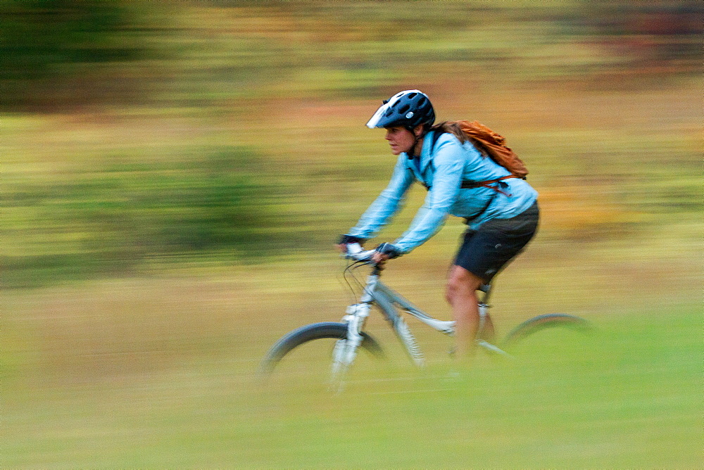 A woman mountain biker is blurred by motion while riding through autumn colors in the Rattlesnake recreation area near Missoula, Montana.