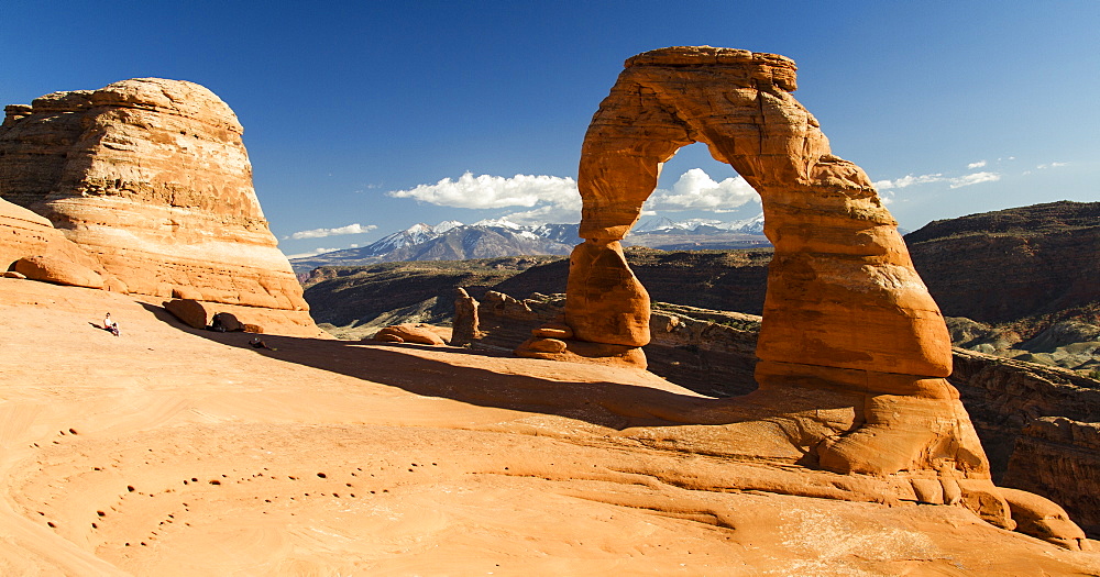 People relaxing while viewing  Delicate Arch with the La Sal mountain range in the background, Arches National Park, Utah.