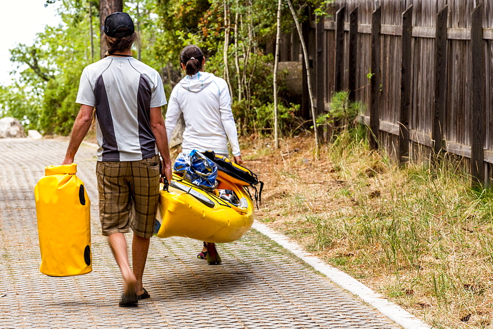 Two people carrying a kayak and drybags down an alley.