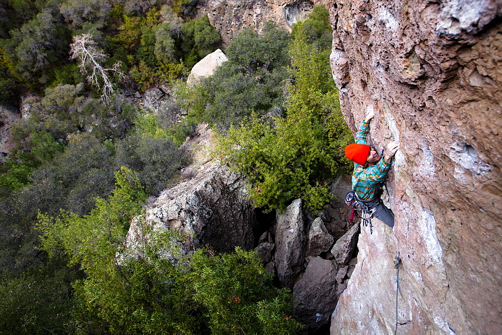 A male climber in an orange beanie and multicolored shirt climbs Family Jewel (5.10d) on Mount Gorgeous in Malibu Canyon State Park in Malibu, California.  Family Jewel is a very popular sport climb in Malibu Canyon.