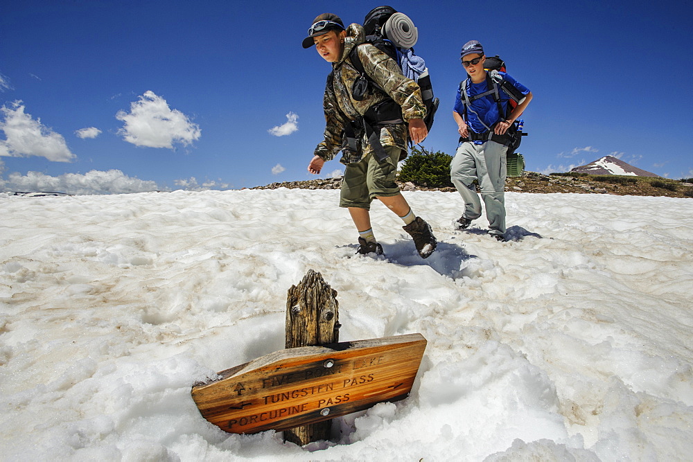 Boys hike past a trail sign buried in a late melting snow field, at about 11,000 feet below Tungsten Pass, on the fourth day of Troop 693's six day backpack trip through the High Uintas Wilderness Area, Uintas Range, Utah