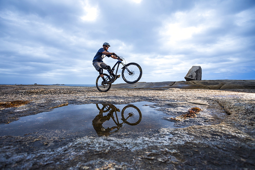 Male mountain biker riding on rocky foreshore near Bicheno blowhole on Tasmania's East Coast.