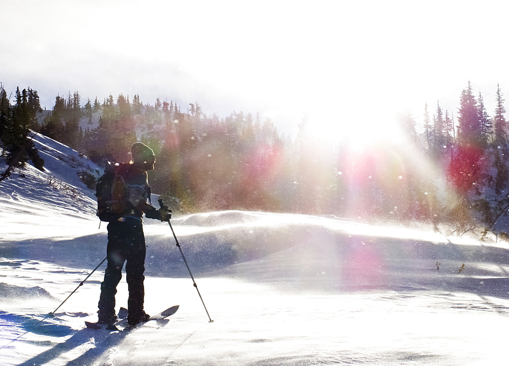 A man splitboarding stops and takes a look into the distance while the sun shines on him.