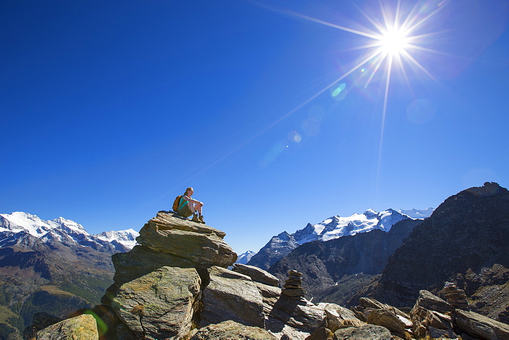 A female hiker sitting on top of the Wannihorn in the Swiss Alps. In the background the four thousand meter peaks of the Weisshorn and Weissmies. This region of Wallis is a outdoor paradise for all climbers, hikers, mountainbikers, trailrunners and nature lovers.