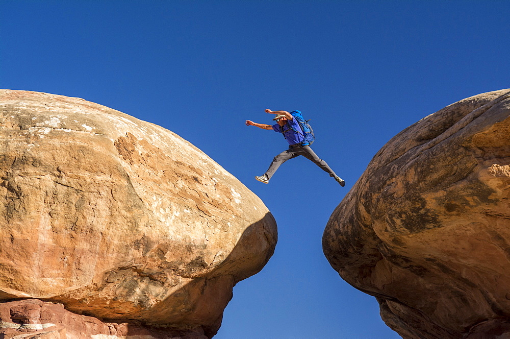 A man jumping between sandstone hoodoos along the Chessler Park and Joint Trail hike, Needles District, Canyonlands National Park, Monticello, Utah.