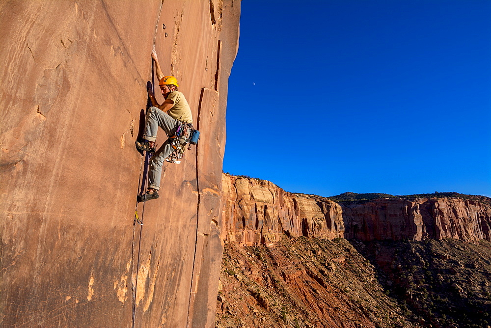 A man rock climbing up a difficult crack called Sig Sauer at the Pistol Whipped Wall in Indian Creek, Monticello, Utah.