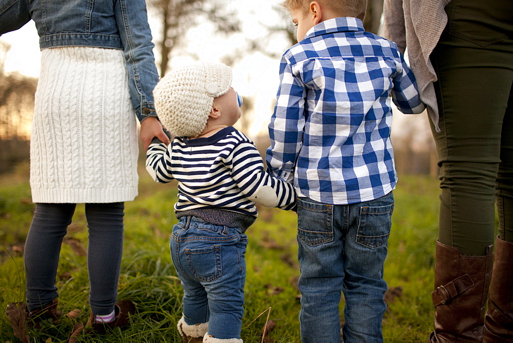 A baby girl looks up at her older brother while walking in a grassy field.