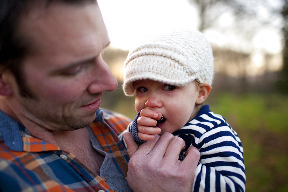 A father holds and comforts his young daughter while she cries.