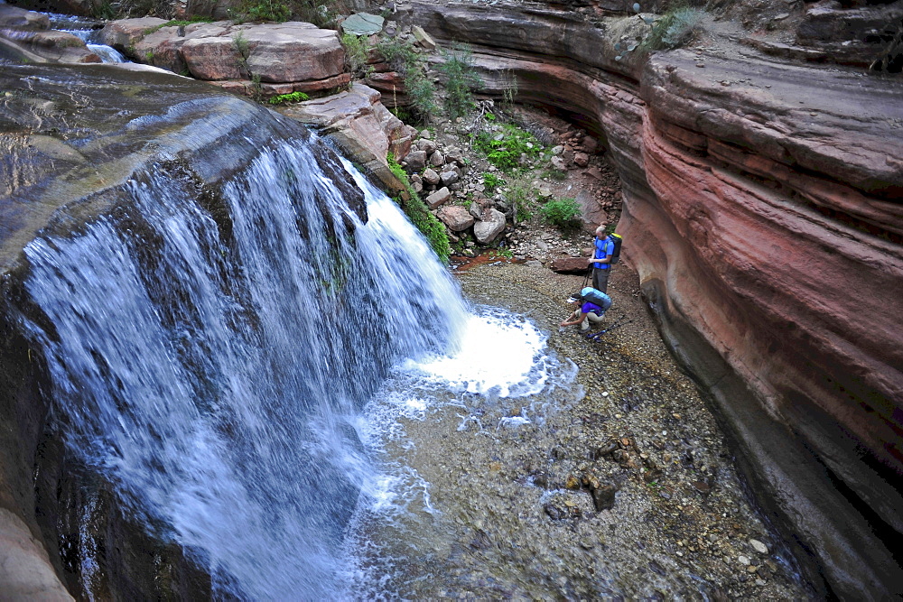 Hikers past small waterfalls along  Deer Creek Narrows in the Grand Canyon outside of Fredonia, Arizona November 2011.  The 21.4-mile loop starts at the Bill Hall trailhead on the North Rim and descends 2000-feet in 2.5-miles through Coconino Sandstone to the level Esplanada then descends further into the lower canyon through a break in the 400-foot-tall Redwall to access Surprise Valley.  Hikers connect Thunder River and Tapeats Creek to a route along the Colorado River and climb out Deer Creek.