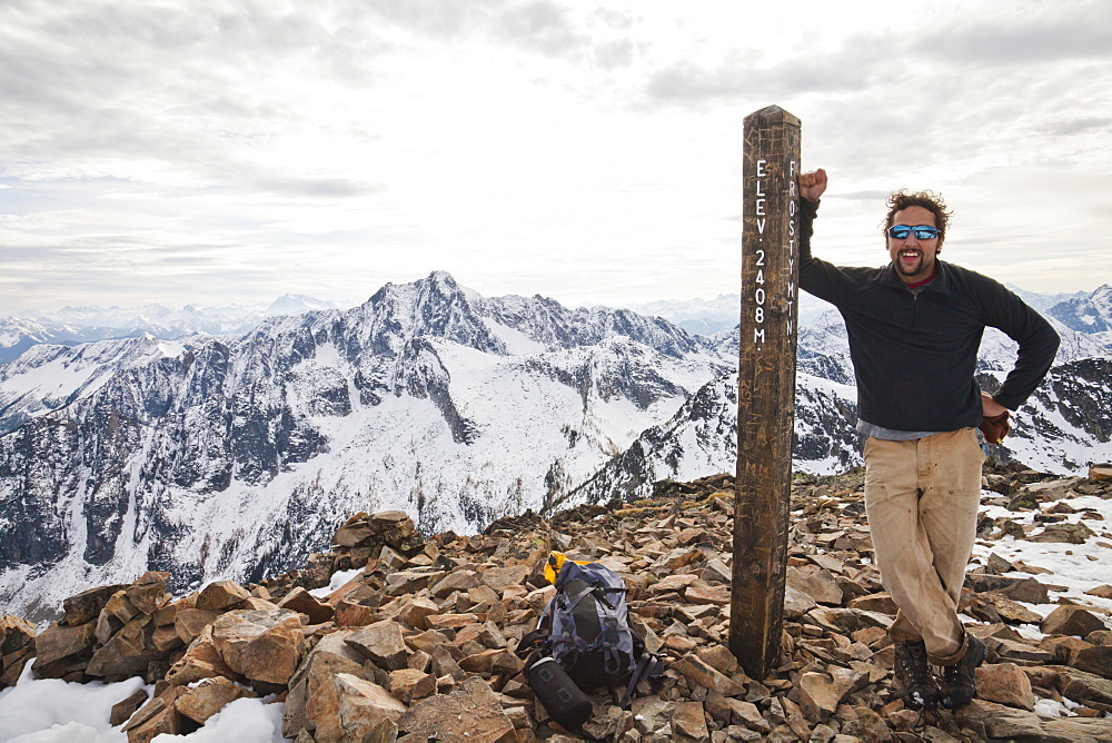 A hiker poses beside the summit post of Frosty Peak, British Columbia, Canada.