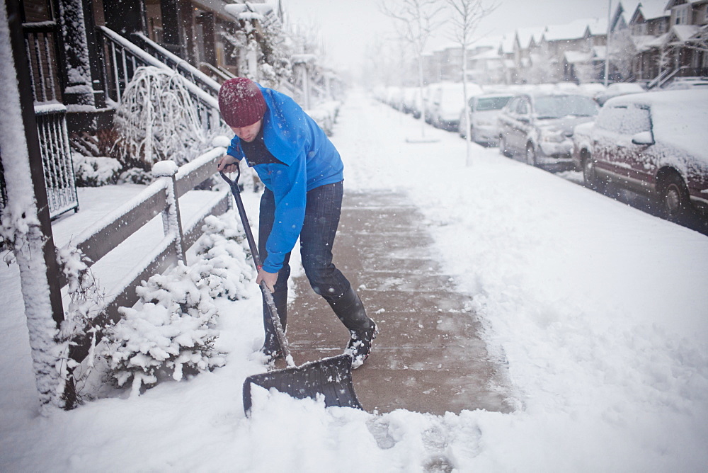 A man shovels the sidewalk outside of his suburban house during a snow storm.