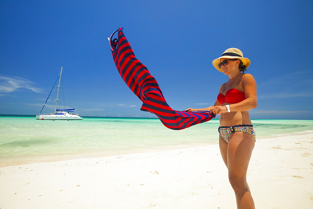 A young woman wearing a bikini shakes the sand off her summer dress while enjoying a beautiful beach in Cuba.