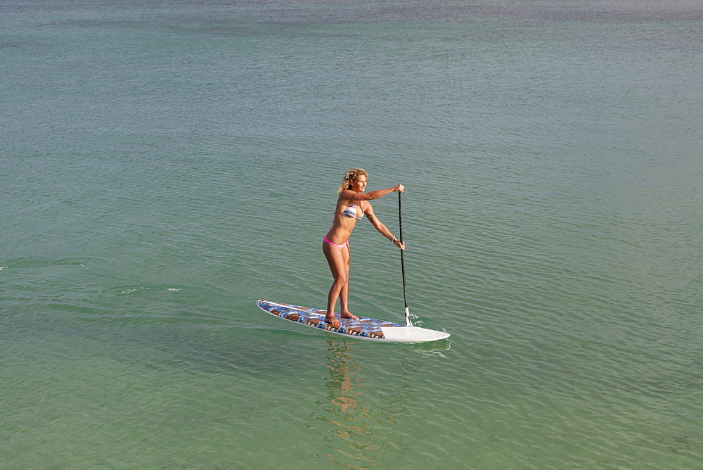 View of a pretty blonde girl in bikini paddling on a stand up paddle board