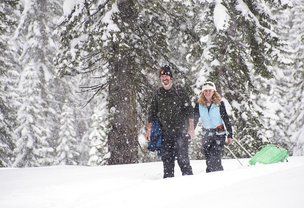 Smiling man and woman snowshoeing in snow storm, Sierra Nevada