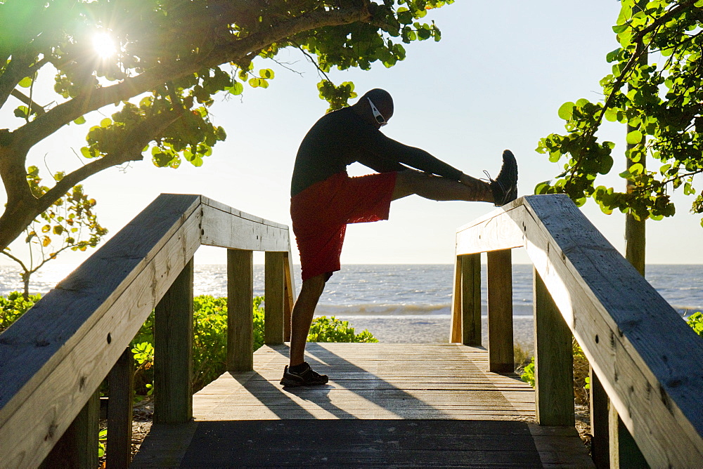 Man stretching on a beach boardwalk