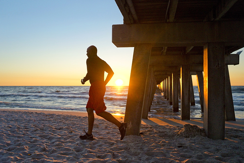 Man running under a pier on the beach at sunset