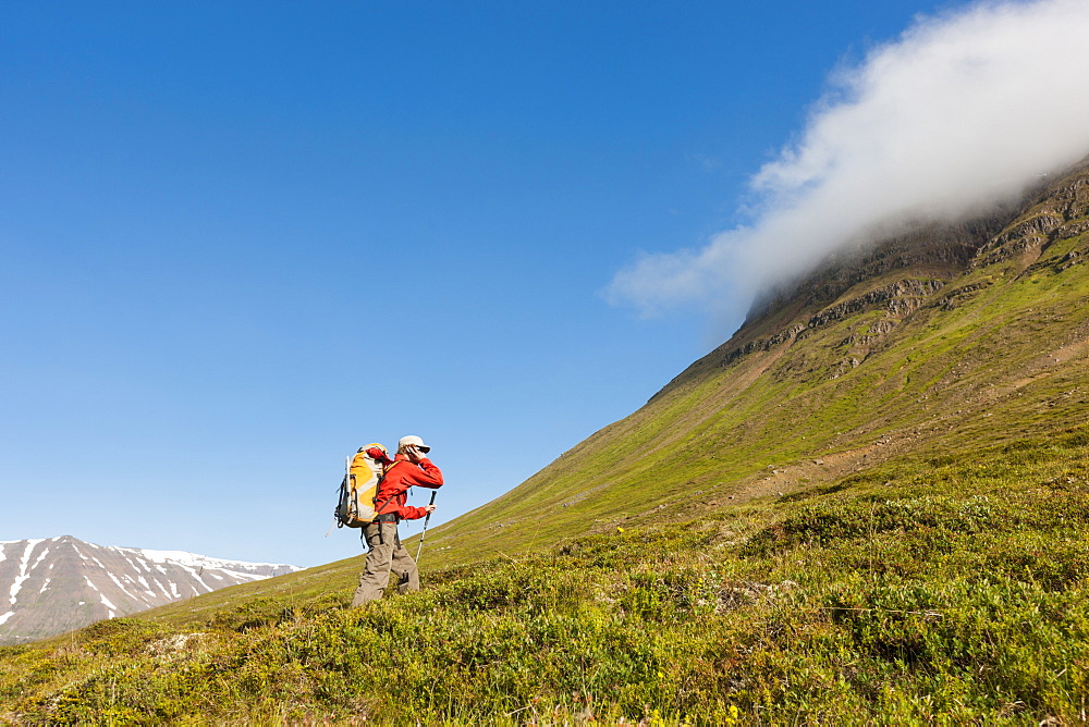 Climber talking on a phone while hiking to a nearby climbing route, north Iceland.