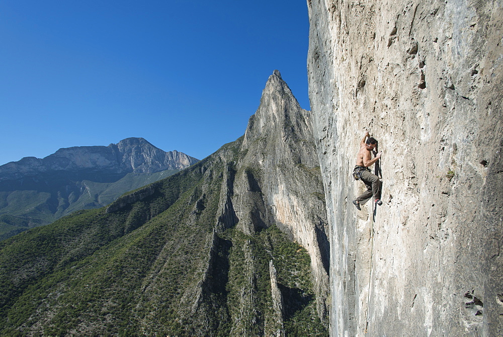 A man climbs up a limestone wall, with one of Potrero Chico's spires on the background.