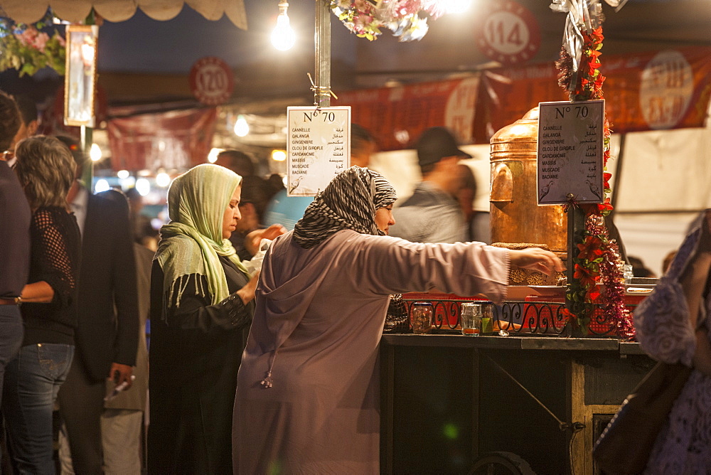 Two Women (40-50-60 years old) with the typical arabic dress (djellaba) at a food stall in Jemaa EL Fna square in Marrakesh, Morocco.