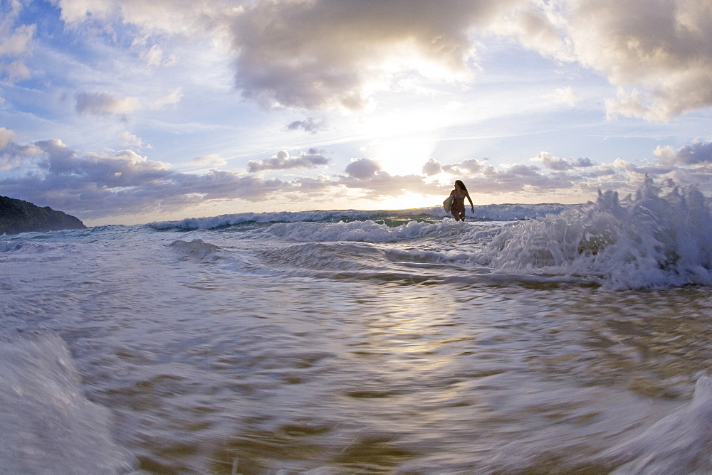 A young woman stand in the surf at sunrise. Blueys Beach, Australia, Australia