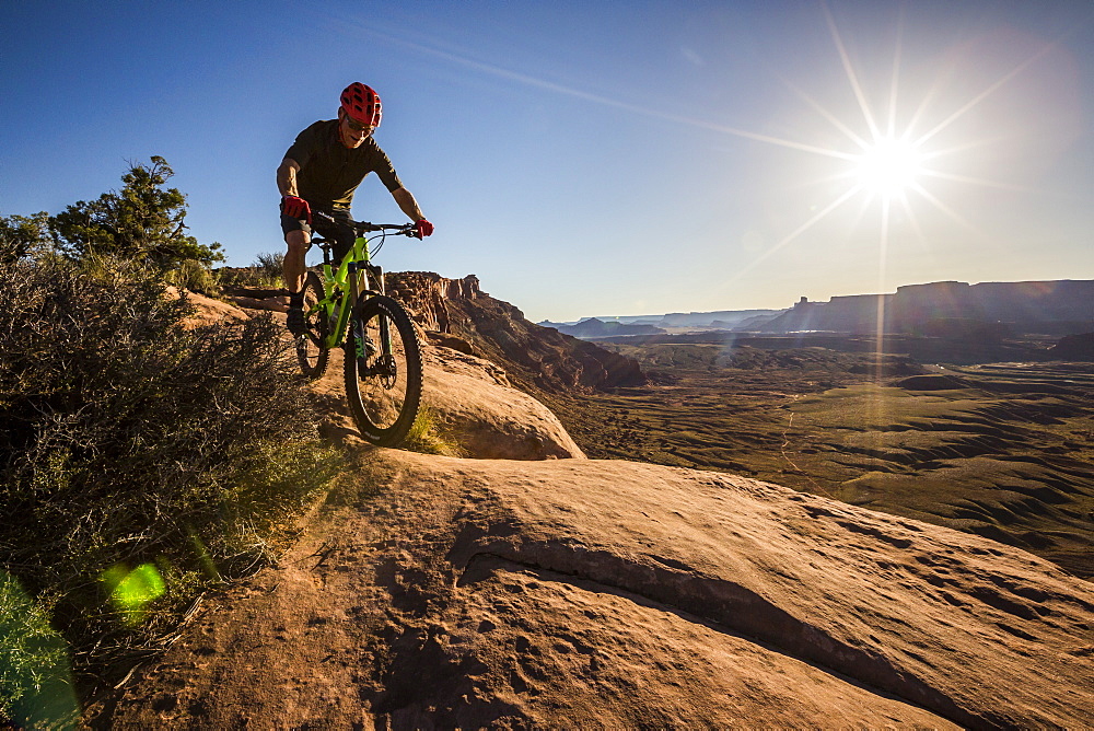 Man mountain biking on a trail in a desert environment at sunset.