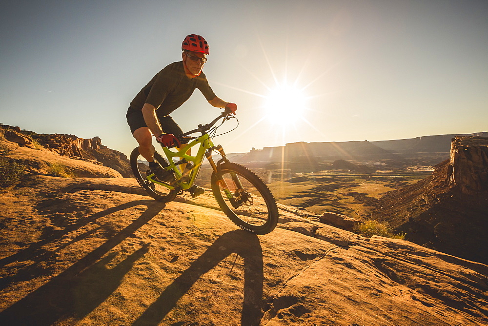 Man mountain biking on a trail in a desert environment at sunset.