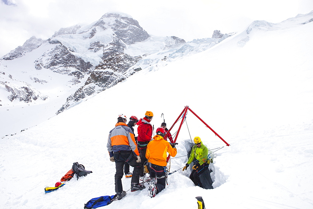 A mountain rescue technician is descending into a crevasse. When a skier breaks through the snow and tumbles down, the only way out is being winched out by the rescuers of Air Zermatt. In the background is the Breithorn mountain.