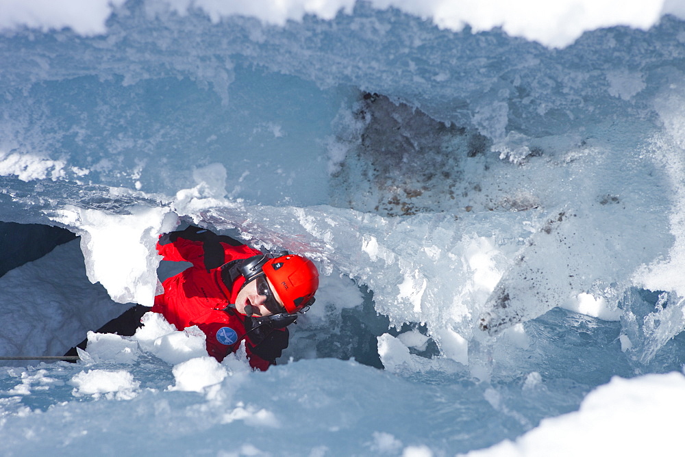 A mountain rescue paramedic is far down in a glacier crevasse, looking up to the surface. In winter the mountain rescue service comes to aid when skiers or climbers tumble down in a hidden crevasse.