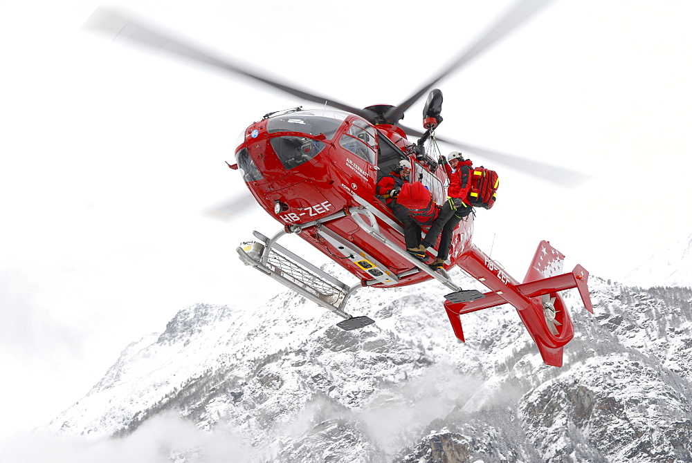 An emergency doctor, patient and paramedic are hanging outside a helicopter during a rescue mission for an injured ski mountaineer.