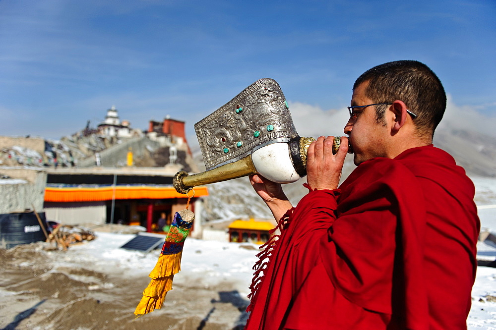 A monk playing Tibetan conch shell horn (dungdkar) on a roof of Spitok Monastery, Ladakh, India.