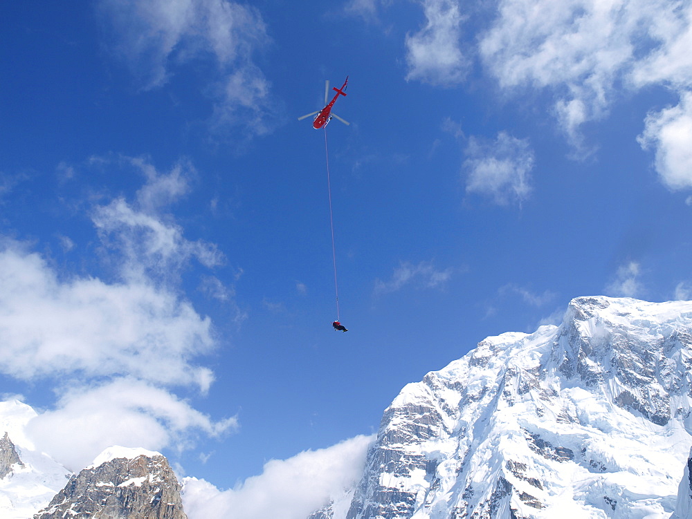 Mountain Ranger is hanging on a long line underneath a helicopter in Denali National Park, Alaska.