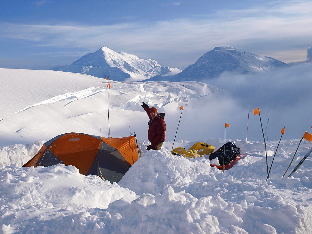 Climber and ranger Brian Scheele is standing next to his tent and pointing to Mount Foraker from 12.000 feet camp high on Mount McKinley.