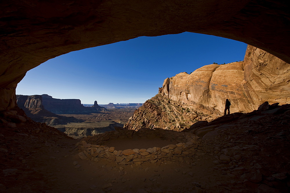 Person standing in alcove near indian ruin with view of desert, Canyonlands National Park, Utah.