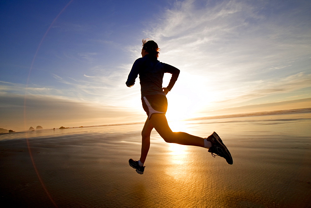 A woman jogs along the wet sand during a beautiful sunset.