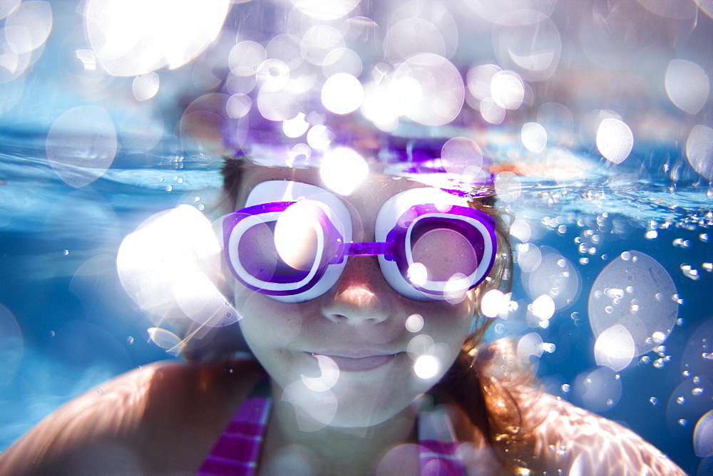 girl swimming in a pool looking at the camera wearing goggles