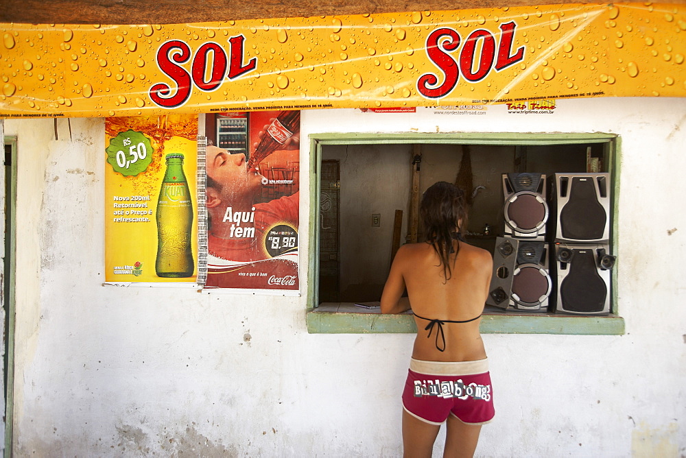 Girl in bathing suit waits at a local shop window, Brazil, north east.