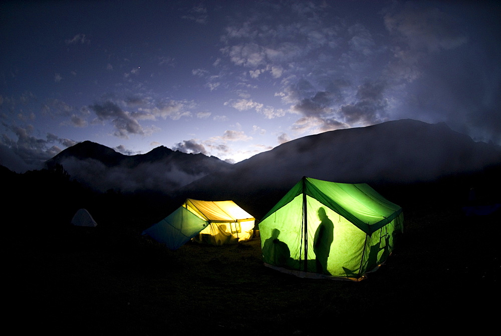 Resting at the foot of mountains, tents glow with light.