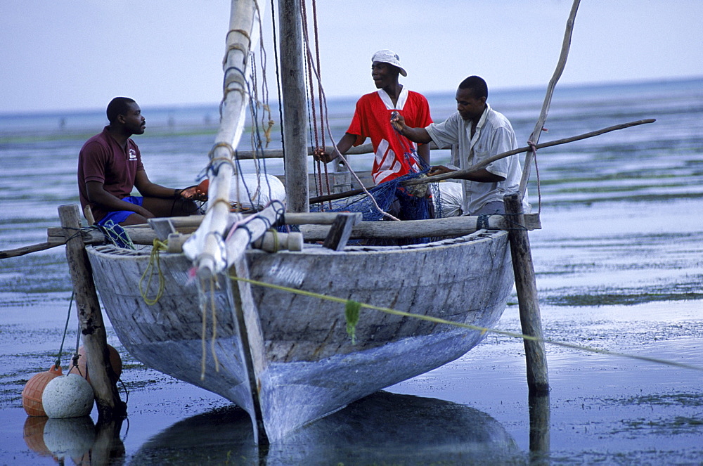 Fishermen sit in a beached dhow on the beach at Paje, on the east coast of Zanzibar Island, Tanzania.