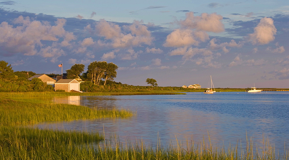 The sun rises over a small harbor where boats are anchored.