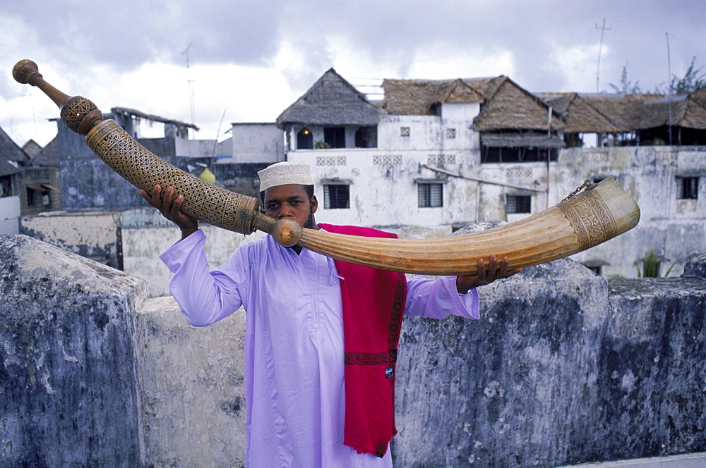 Swahili man blowing the ivory Pate Siwa, a horn carved from an elephant tusk (ivory). On a rooftop in Lamu town on Lamu, an island in the Indian Ocean off the northern coast of Kenya