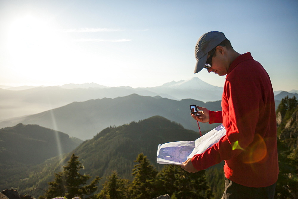 A man uses a compass and paper map to navigate while hiking in the North Cascade Mountain Range, North Cascades National Park, Washington, United States of America