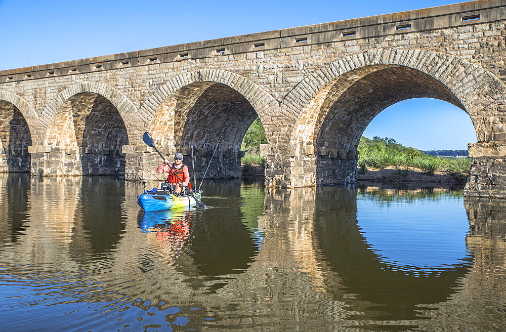 Angler paddles under a bridge on the Brazos River
