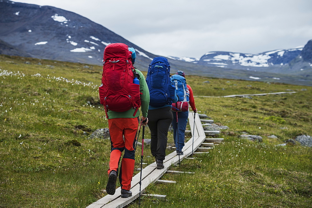 Hikers walk on wooden planks between Alesjaure and Tjäktja, Kungsleden trail, Lapland, Sweden