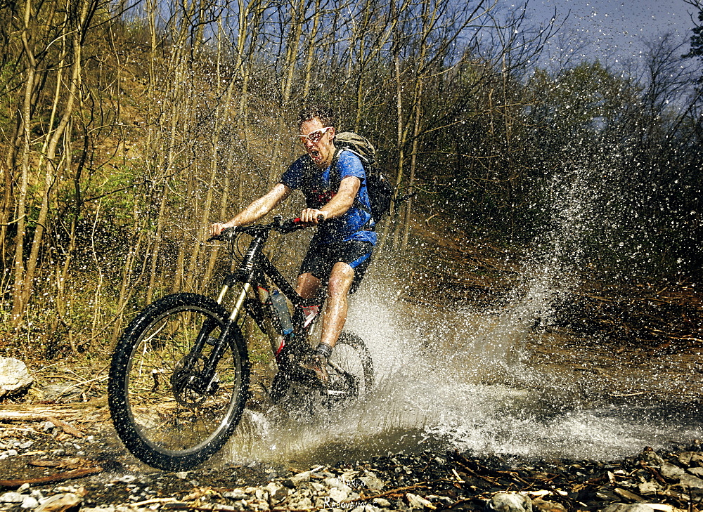 Guy rides his mountain bike over mountain stream. Image captured at the moment of a biggest splash. Taken on Gledic mountains near Kragujevac, Central Serbia at a sunny Spring day.